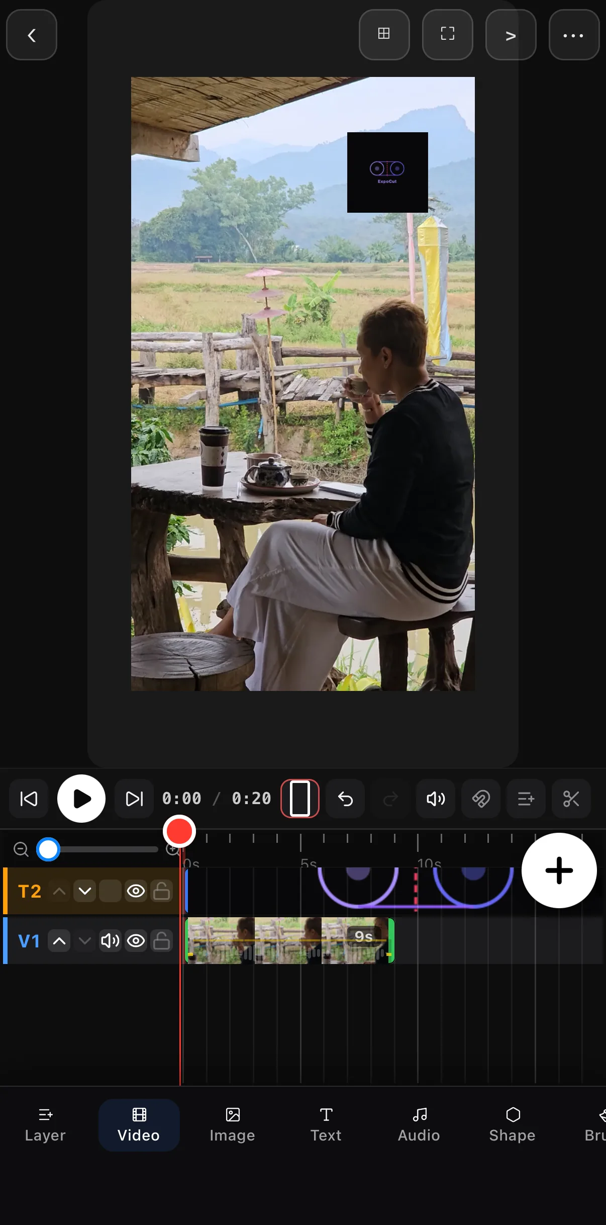 A 9:16 coffee-shop clip with a small ExpoCut logo layer placed in the top-right corner; the timeline shows the logo on T2 above the video on V1.